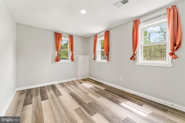 spare room with a wealth of natural light, wood finished floors, visible vents, and baseboards