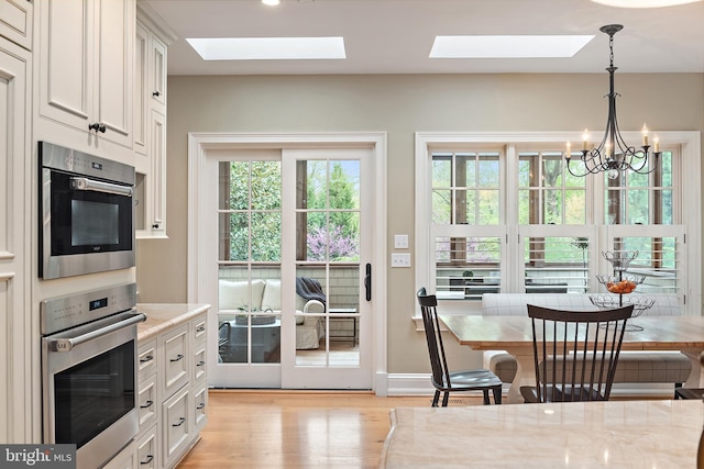 208 Wardour Dr, Annapolis, MD 21401 - kitchen featuring a skylight, light wood-style flooring, white cabinets, and a notable chandelier