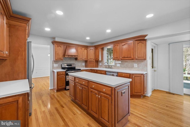 kitchen featuring custom range hood, backsplash, light wood-style floors, brown cabinetry, and appliances with stainless steel finishes