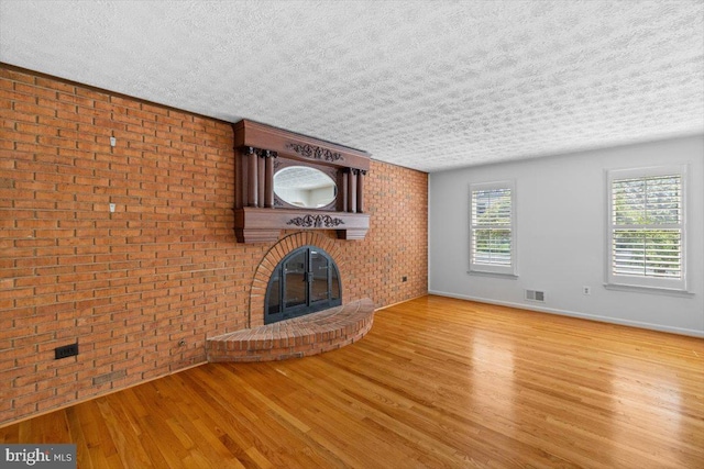 unfurnished living room with brick wall, a fireplace, visible vents, and wood finished floors