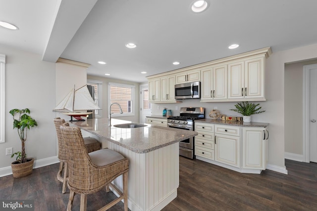 kitchen featuring a sink, appliances with stainless steel finishes, dark wood finished floors, cream cabinetry, and light stone countertops