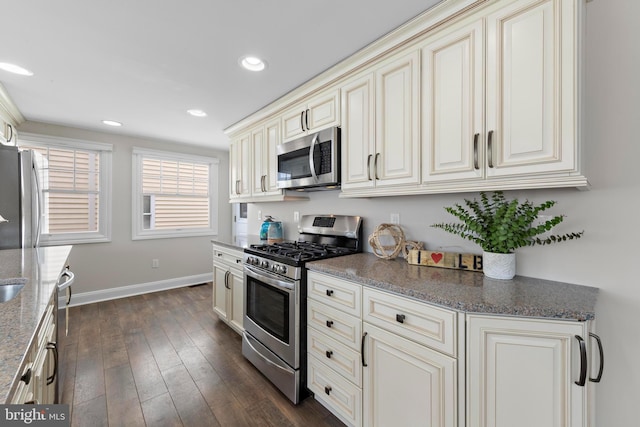 kitchen featuring stone countertops, appliances with stainless steel finishes, dark wood-style flooring, cream cabinets, and baseboards