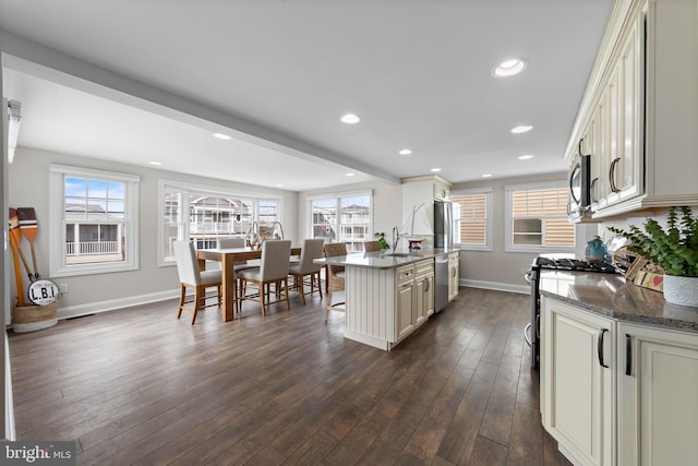 kitchen featuring a kitchen breakfast bar, baseboards, dark wood-style floors, cream cabinetry, and stainless steel appliances