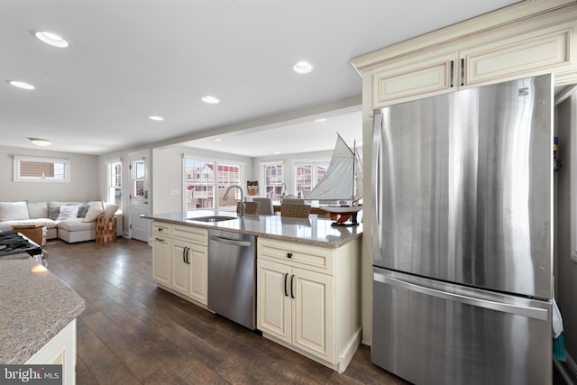 kitchen with a sink, open floor plan, appliances with stainless steel finishes, dark wood-style floors, and cream cabinetry