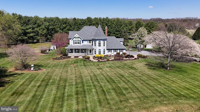 rear view of house featuring a lawn, a porch, a chimney, and a shingled roof