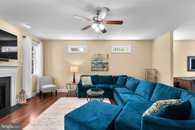 living area featuring baseboards, a ceiling fan, dark wood-style floors, and a fireplace