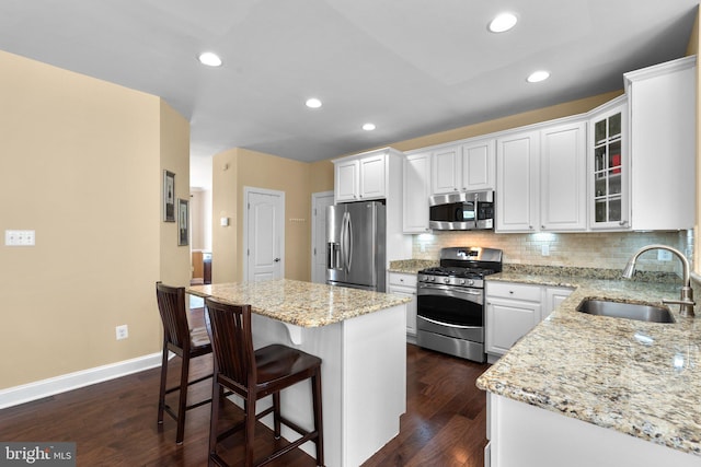 kitchen with a breakfast bar, a sink, a center island, stainless steel appliances, and white cabinetry
