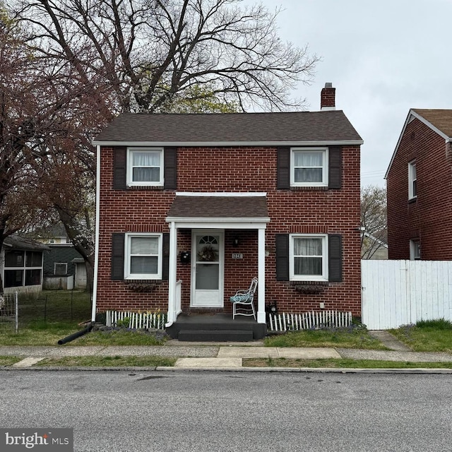 view of front of house with a chimney, brick siding, fence, and roof with shingles