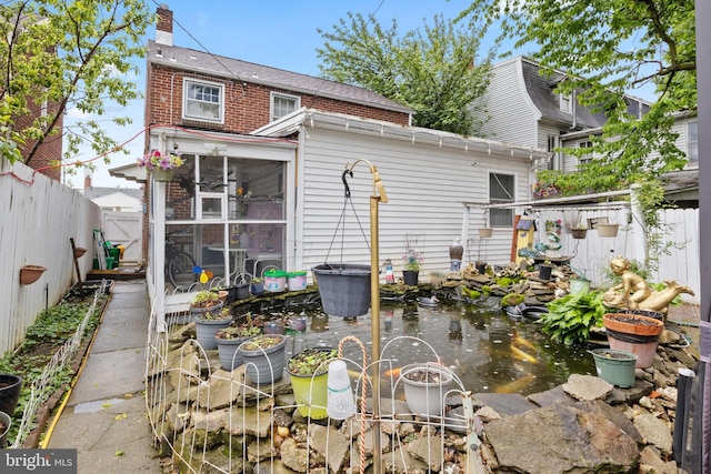 back of property with a sunroom, a fenced backyard, a chimney, and brick siding