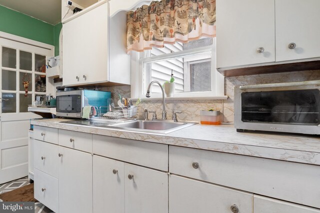 kitchen with stainless steel microwave, light countertops, white cabinets, and tasteful backsplash