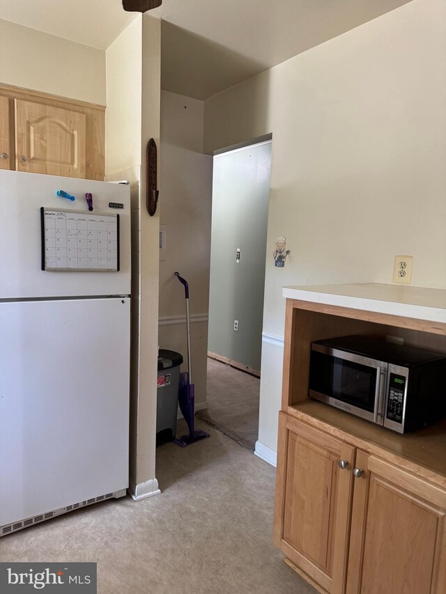 kitchen featuring light brown cabinets, stainless steel microwave, freestanding refrigerator, baseboards, and light colored carpet