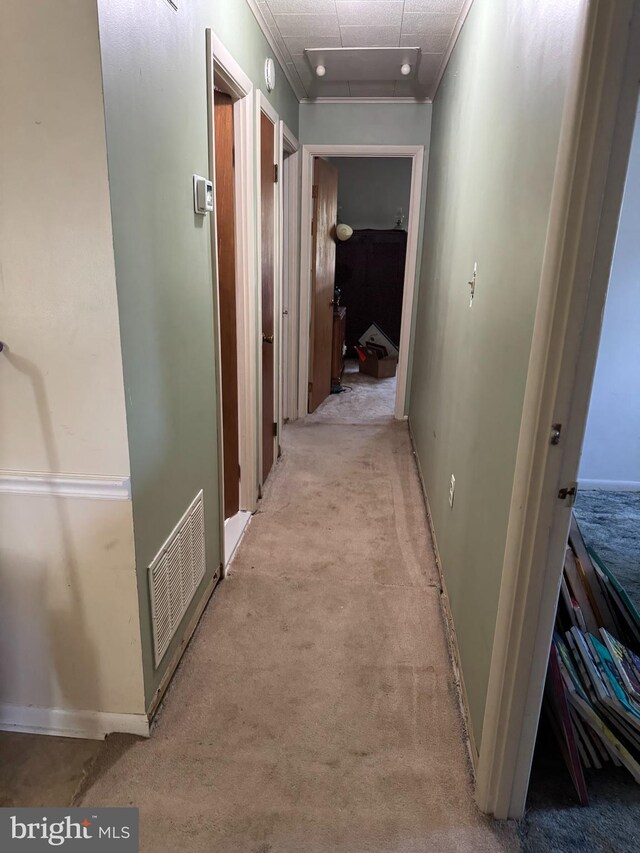 hallway with attic access, crown molding, baseboards, and light carpet