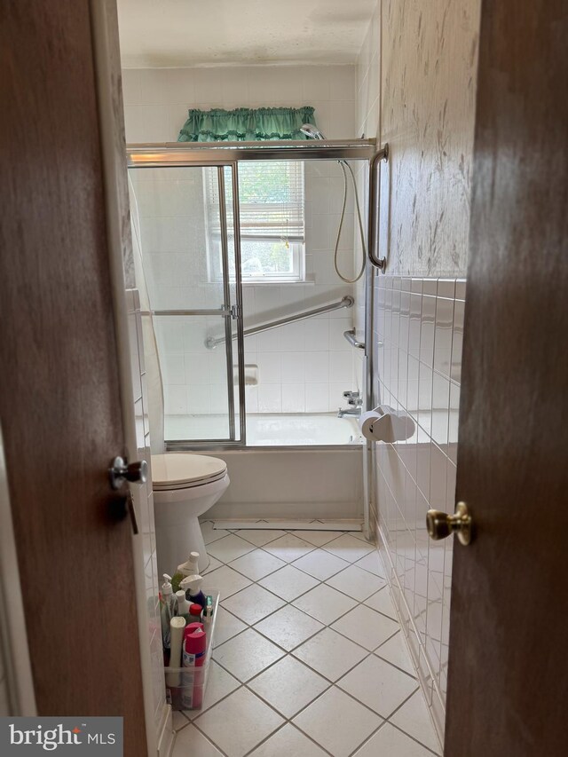 full bathroom with combined bath / shower with glass door, tile patterned flooring, and toilet