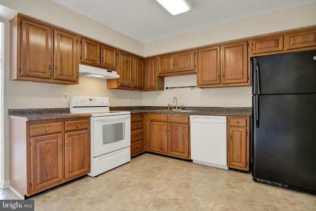 kitchen featuring dark countertops, a sink, white appliances, brown cabinetry, and under cabinet range hood