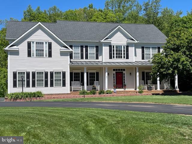 colonial home with a standing seam roof, covered porch, metal roof, and a front yard