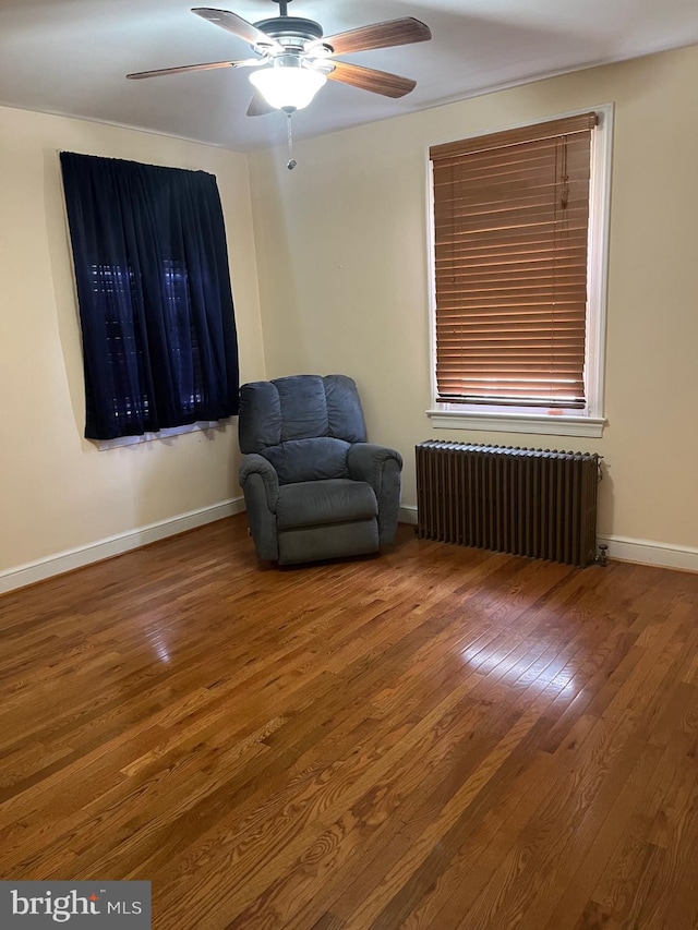 living area with radiator, baseboards, wood finished floors, and ceiling fan