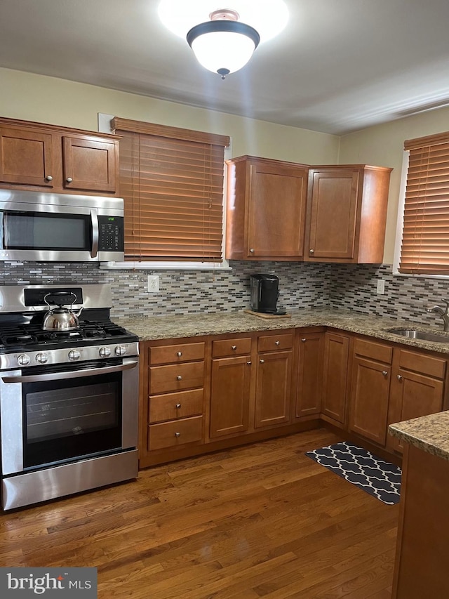 kitchen with wood finished floors, a sink, decorative backsplash, appliances with stainless steel finishes, and light stone countertops