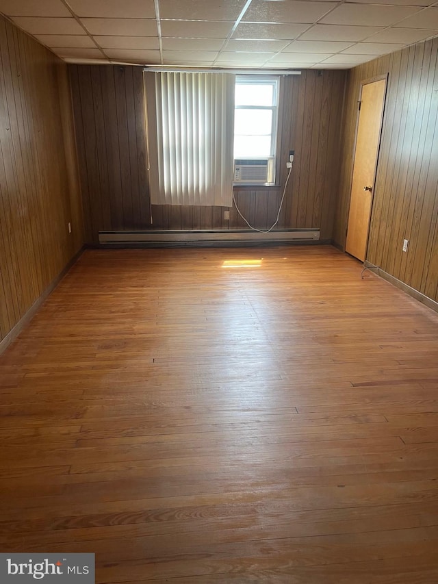 empty room with a baseboard radiator, wood finished floors, wood walls, and baseboards