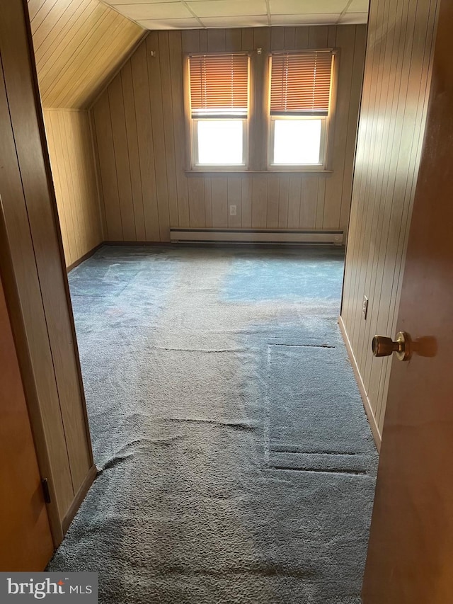 additional living space featuring wood walls, vaulted ceiling, baseboards, a baseboard radiator, and carpet flooring