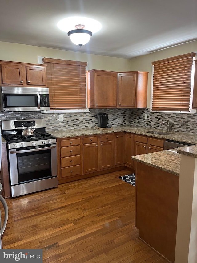 kitchen featuring brown cabinets, backsplash, wood finished floors, a sink, and appliances with stainless steel finishes