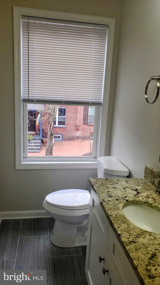 half bathroom featuring toilet, vanity, and baseboards