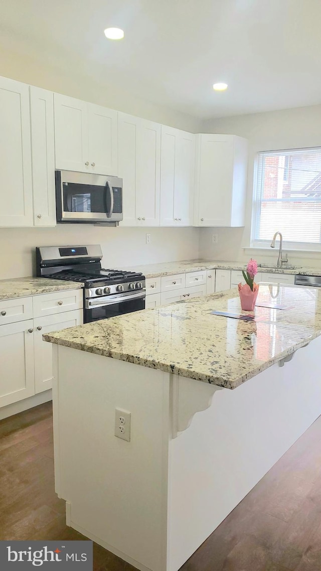 kitchen with a kitchen breakfast bar, white cabinetry, a kitchen island, appliances with stainless steel finishes, and a sink