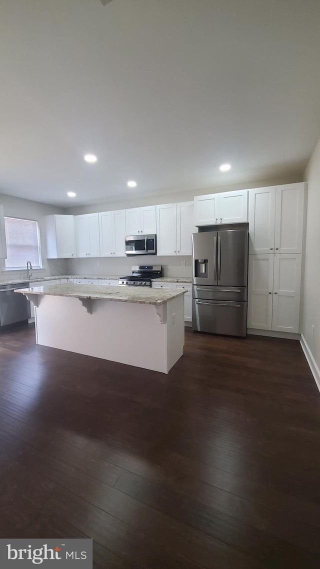 kitchen with dark wood-style flooring, a breakfast bar, light stone counters, white cabinets, and appliances with stainless steel finishes