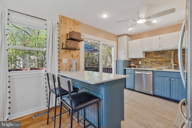 305 W Poplar Rd, Sterling, VA 20164 - kitchen featuring blue cabinetry, decorative backsplash, a peninsula, light wood-style flooring, and appliances with stainless steel finishes