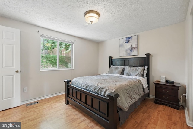 bedroom with wood finished floors, a textured ceiling, and baseboards