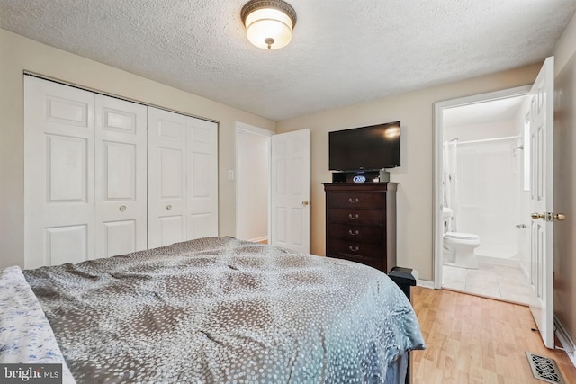 bedroom with a closet, light wood-type flooring, a textured ceiling, connected bathroom, and baseboards
