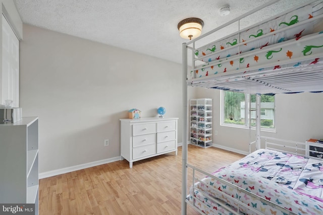 bedroom featuring light wood-type flooring, baseboards, and a textured ceiling