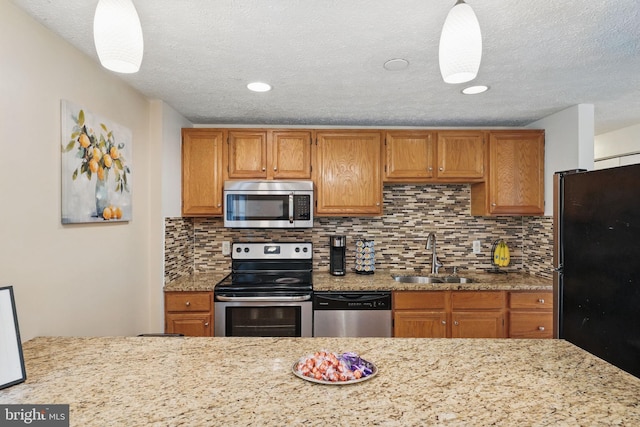 kitchen featuring appliances with stainless steel finishes, a sink, tasteful backsplash, a textured ceiling, and brown cabinetry