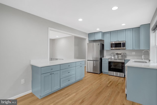 kitchen with light wood-type flooring, recessed lighting, appliances with stainless steel finishes, light countertops, and a sink
