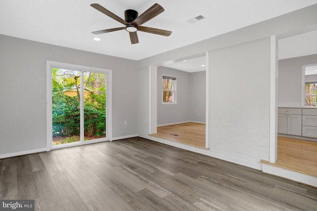 empty room featuring plenty of natural light, visible vents, wood finished floors, and ceiling fan