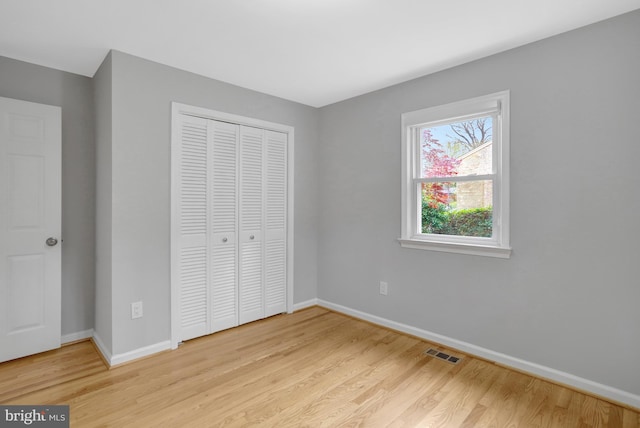 unfurnished bedroom featuring a closet, visible vents, baseboards, and wood finished floors