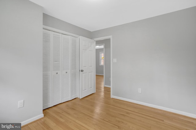 unfurnished bedroom featuring light wood-style flooring, a closet, and baseboards