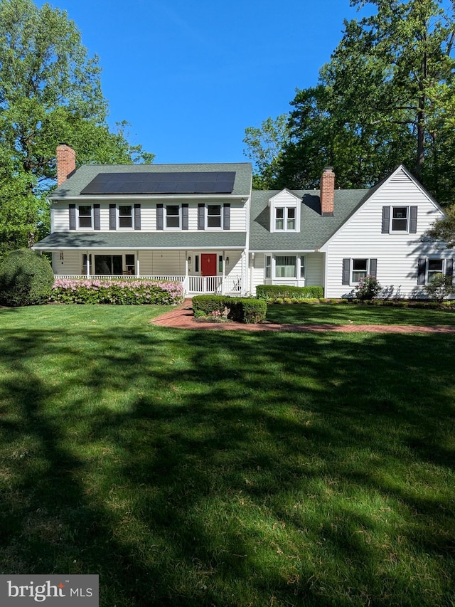 view of front of property featuring a chimney, roof mounted solar panels, a front lawn, and a porch