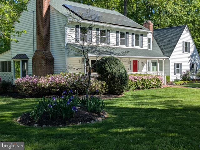 view of front facade with a chimney, solar panels, and a front lawn