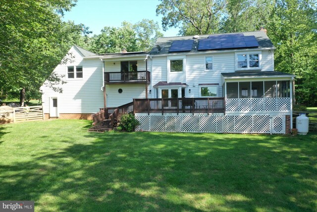 rear view of house featuring a balcony, a sunroom, roof mounted solar panels, a deck, and a chimney