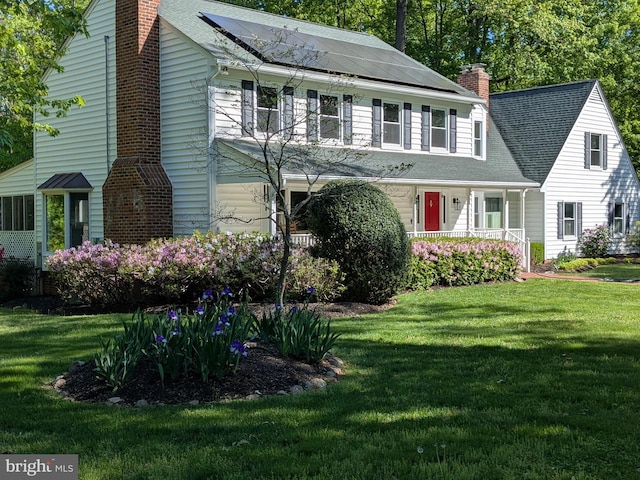 view of front of property featuring a chimney, roof mounted solar panels, a front yard, and a shingled roof