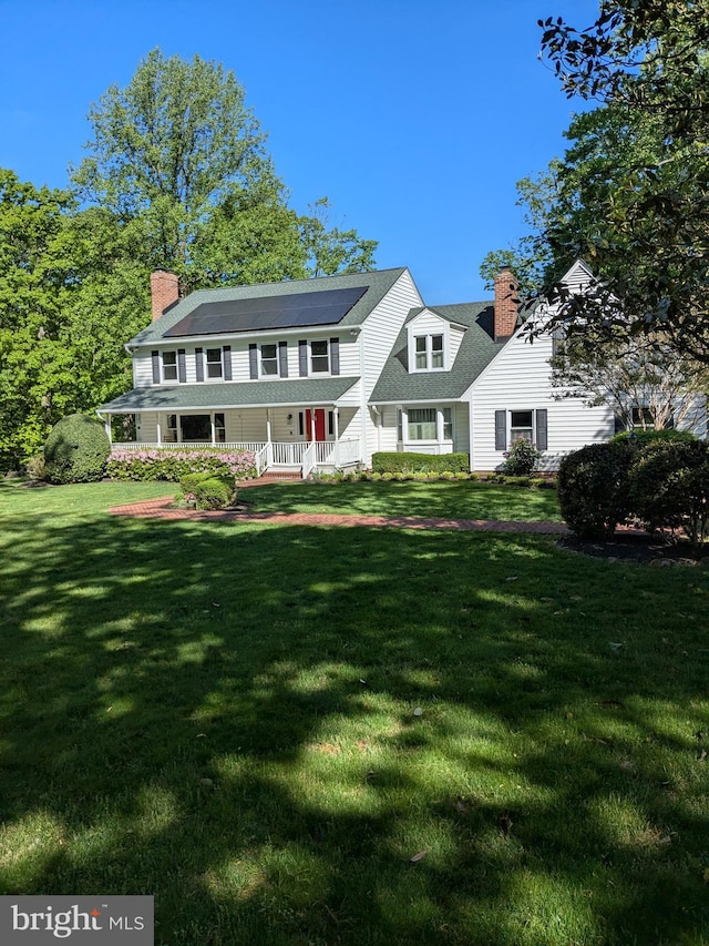 rear view of house featuring a chimney, a porch, a yard, and solar panels