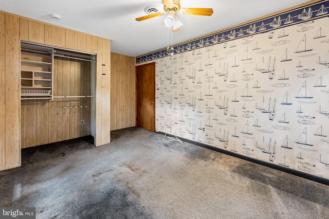 unfurnished bedroom featuring a closet, wood walls, ceiling fan, and carpet floors