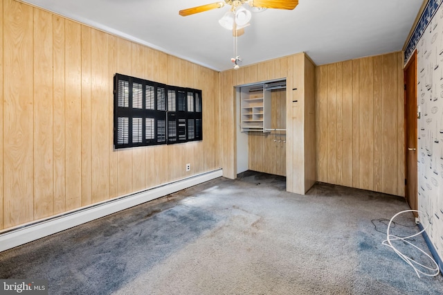 unfurnished bedroom featuring a ceiling fan, baseboard heating, a closet, carpet flooring, and wooden walls