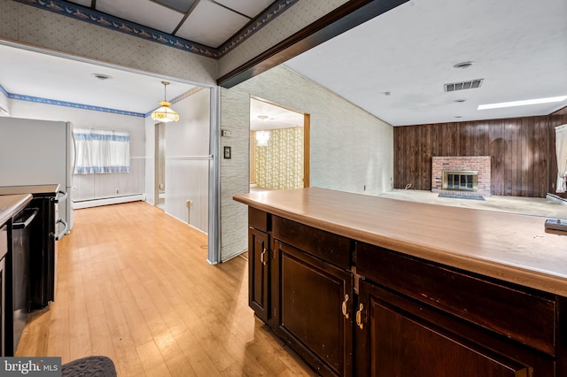 kitchen with a baseboard radiator, wallpapered walls, a brick fireplace, a wainscoted wall, and light wood-type flooring