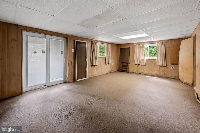 interior space featuring a paneled ceiling, wooden walls, carpet flooring, and plenty of natural light