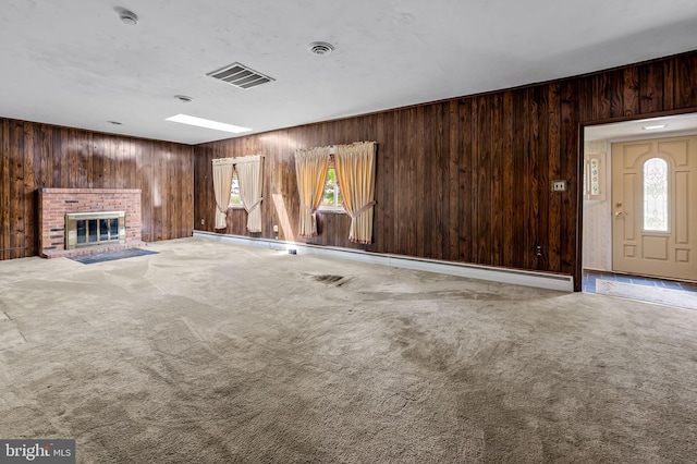 unfurnished living room with carpet flooring, wooden walls, visible vents, and a brick fireplace
