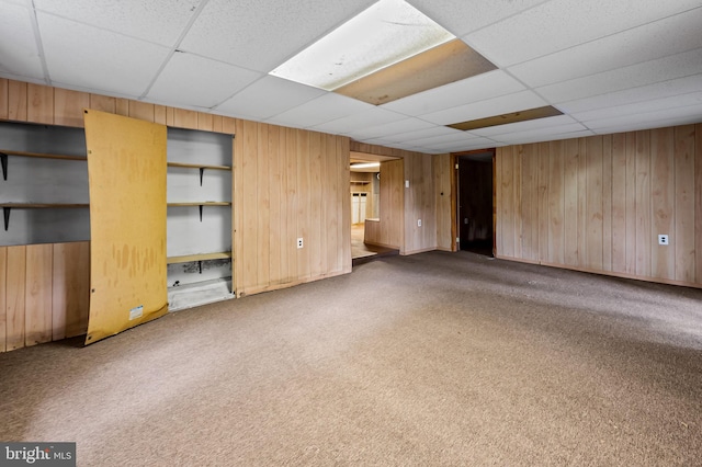 unfurnished living room with wooden walls, carpet, and a drop ceiling