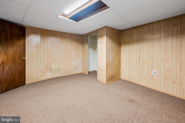 finished basement featuring a drop ceiling, carpet flooring, and wood walls