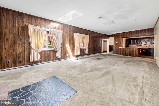 unfurnished living room featuring a sink, a skylight, carpet flooring, and wood walls
