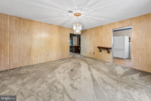 carpeted spare room featuring wooden walls, a notable chandelier, and visible vents